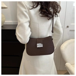 Detail einer dunkelbraunen Tasche mit Krokodilmuster und Silberschnalle an einem Model