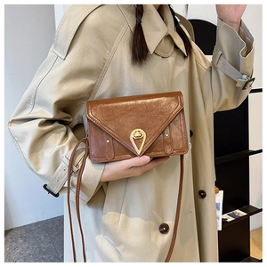 Detail of a brown leather envelope bag with a golden teardrop twist lock on a beige coat