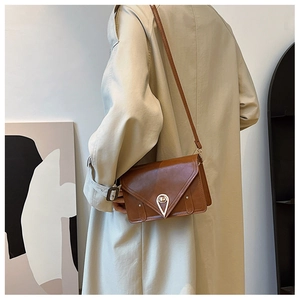 Close-up of tan crossbody bag featuring a teardrop lock on a beige trench coat