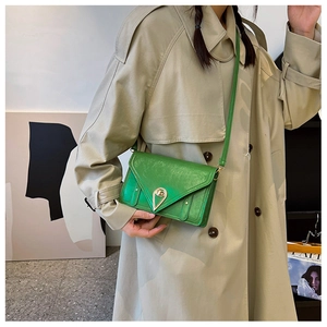 Detail of a bright green crossbody bag with a gold triangular buckle on a khaki coat