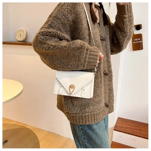 Close-up of white envelope shoulder bag featuring a golden triangle buckle and leather texture