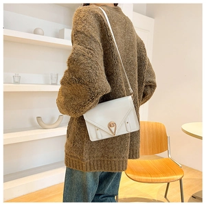 Detail of a white envelope crossbody bag with a gold heart-shaped rotating lock on a sweater