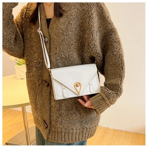 White envelope crossbody bag with golden water drop lock detail on a knit sweater