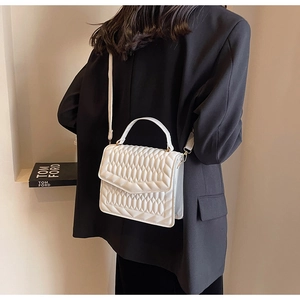Witte gewatteerde crossbodytas met gouden hardware gedragen door een model in het zwart