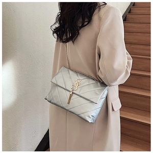 Détail du sac matelassé argenté avec logo doré et pompon sur la bandoulière chaîne