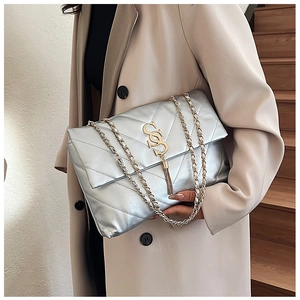 Sac bandoulière argenté matelassé avec logo doré et pompon élégant porté sur un trench