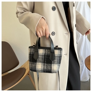 Detail of checkered wool handbag with black leather trim held by a model in a beige suit
