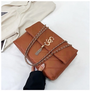 Détail du sac matelassé marron avec logo doré et pompon sur fond de tissu beige