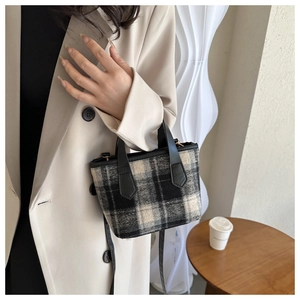 Detail of checkered wool handbag with black leather handles styled with a beige blazer
