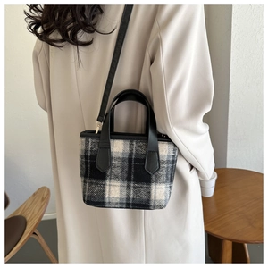 Detail of vintage plaid bucket bag with black leather handles on a beige autumn coat