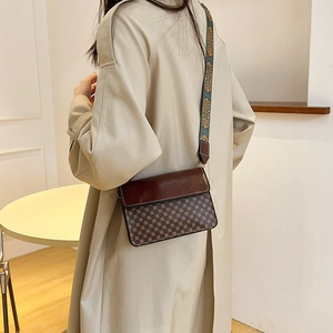 Vintage patterned crossbody bag with wide jacquard strap worn by a model in a trench coat