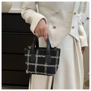 Detail of black tweed plaid handbag with leather straps and metallic D-ring buckle