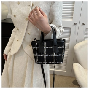 Close-up of elegant black tweed bucket bag with textured woven pattern and leather handle