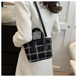 Detail of black tweed bucket bag featuring intricate woven patterns on a model wearing white coat