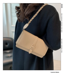 Detalle de un bolso bandolera rectangular beige con correa tejida gruesa y acabado mate
