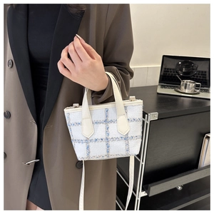 Close-up of blue and white tweed handbag with leather handles on a minimalist desk