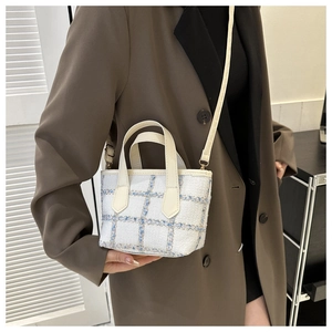 Detail view of a cream tweed plaid handbag worn by a model in a brown blazer