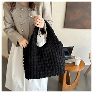 Détail du sac cabas noir à texture gaufrée tenu par un mannequin dans un bureau