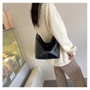 Close-up of black glossy leather tote bag with a vintage patterned wide shoulder strap