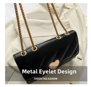Detail of black quilted crossbody bag with heart buckle and gold metal eyelet design