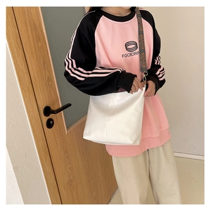 Detail view of a white leather crossbody tote bag styled with a sporty casual sweatshirt