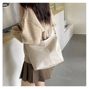 Detailed view of off-white leather tote bag with lychee texture and gold metal buckle