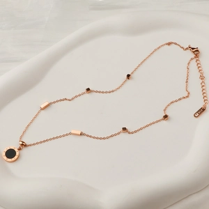 Rose gold stainless steel love necklace with black circular pendant on ceramic tray