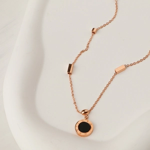 Close-up of rose gold necklace with black circular pendant and LOVE engraving detail