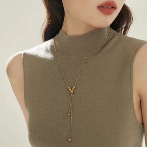 Adjustable Y-shaped gold ball tassel necklace displayed on a green turtleneck sweater