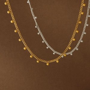 Colliers minimalistes dorés et argentés avec de petites boules métalliques sur fond texturé