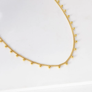 Détail d'un collier doré délicat orné de perles minimalistes et pendentifs ronds