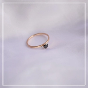 Macro detail of minimalist rose gold ring with a four-prong set black gemstone