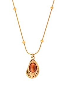 Détail du pendentif en œil de tigre doré avec bordure irrégulière et chaîne à billes dorées