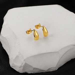 Minimalist golden teardrop stud earrings with polished mirror finish on stone stand