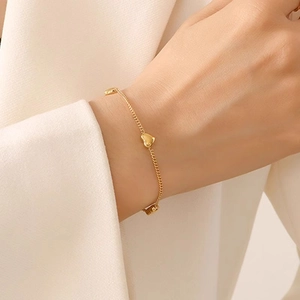 Elegant gold curb chain bracelet with three heart pendants on a beige blazer background