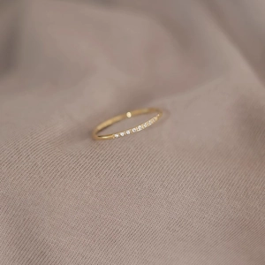 Anillo minimalista de titanio chapado en oro con circonitas sobre un fondo de tela