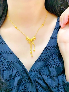 Détail d'un collier doré à nœud et pompons porté sur une robe noire à col en V brodée