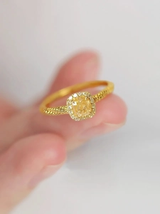 Détail d'une bague avec gemme jaune coupe radiant, halo de diamants et anneau torsadé