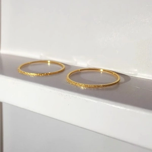 Minimalist ultra-thin gold sandblasted rings set on a white tiered background pedestal
