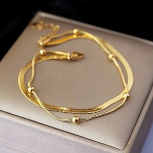 Elegant double-layered gold titanium anklet featuring flat snake chain and polished beads