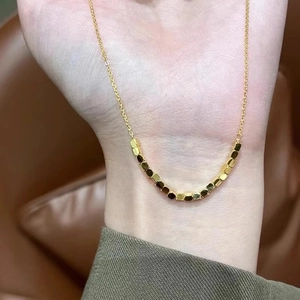 Minimalist gold necklace with geometric square beads shown on a hand against leather