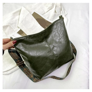 Detail of dark green oily leather tote with a colorful bohemian woven shoulder strap