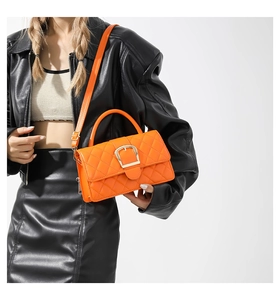 Détail du sac matelassé orange vif avec boucle dorée sur une veste en cuir noir