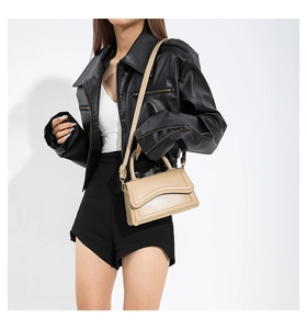 Detail of a beige crossbody bag with wavy flap and adjustable strap on a leather jacket