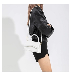White minimalist crossbody bag with wavy flap design shown on model shoulder