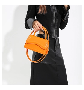Close-up of bright orange crossbody bag with magnetic flap and handle on black outfit