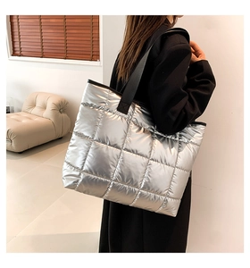 Detailed side view of silver quilted tote bag with black straps in modern interior