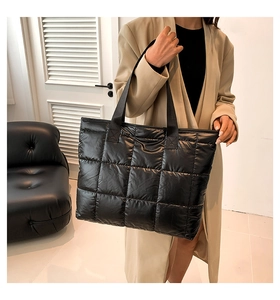 Detail of a large black quilted tote bag with padded grid pattern worn with a trench coat