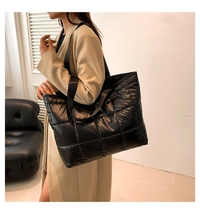 Detail of a large black quilted tote bag with glossy finish and square padded patterns