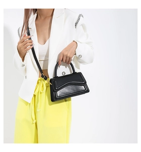 Detail of black wave-design leather bag with gold hardware held by a model in a suit